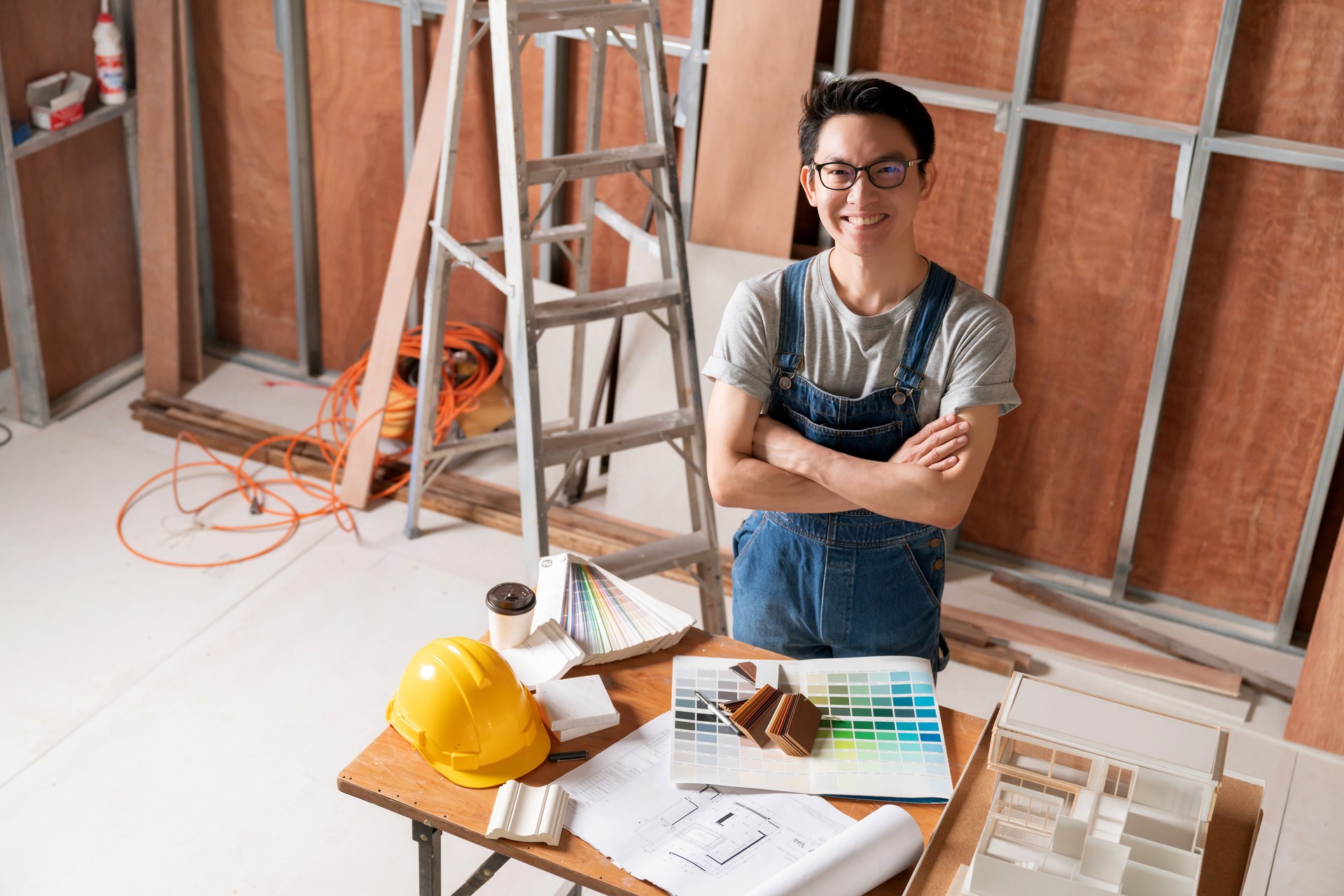 asian attractive glasses interior designer working at house site renovation construction progress with smile and confident at desk with blue print and drawing tool